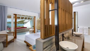 A modern hotel room with a large bed, a sitting area with a view of the sea, a large bathroom with a freestanding sink, and a wooden vanity.