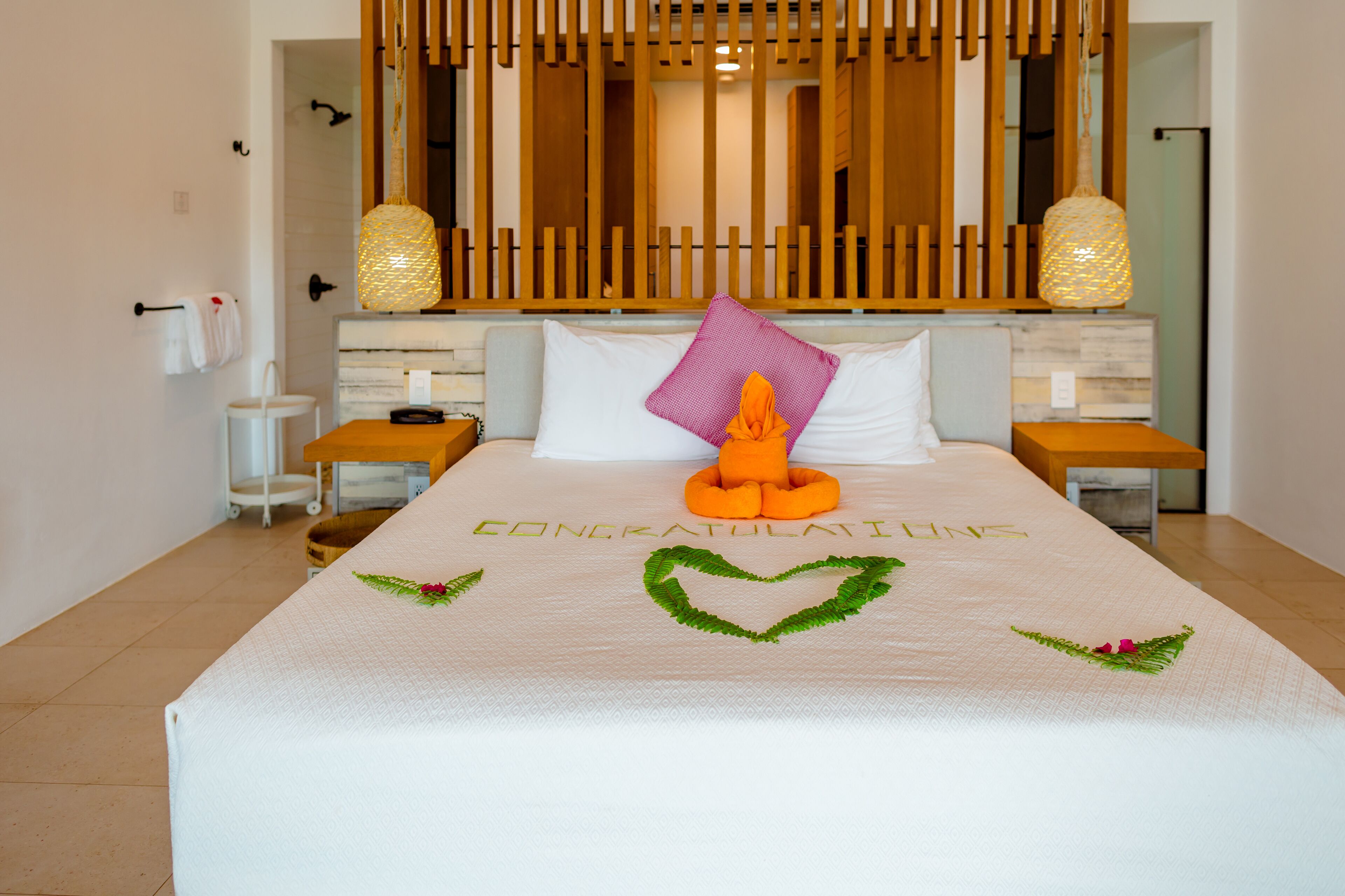 A neatly made bed with a 'CONGRATULATI' sign, a decorative pillow, and a heart-shaped decoration.
