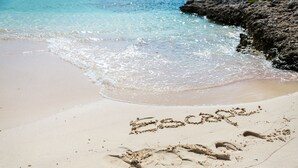 A beach with footprints and the word "Escape" written in the sand.