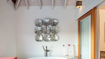 Een moderne badkamer met een vrijstaand bad, een decoratief wandobject en een houten plafond.