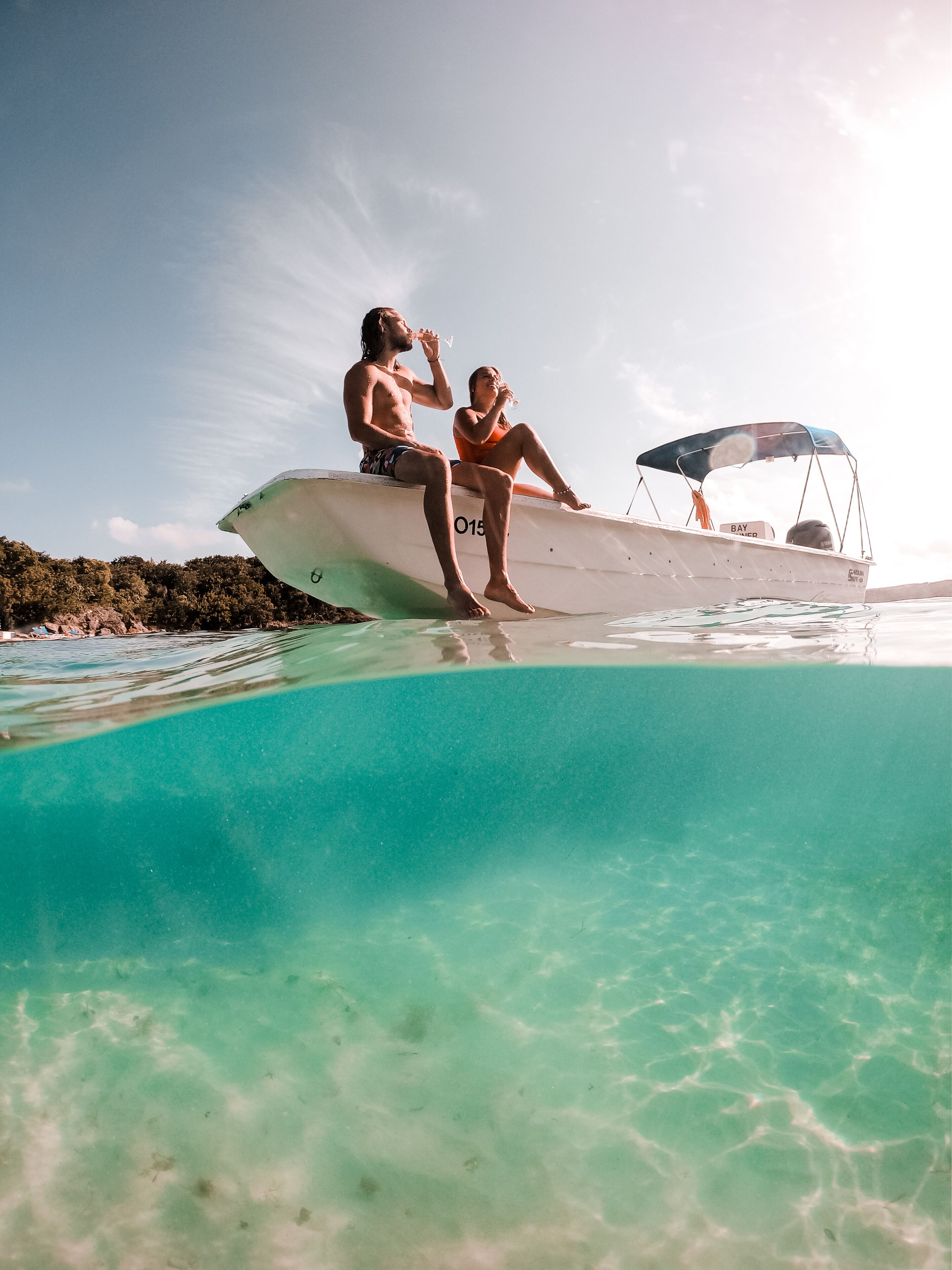 Un bote con dos personas sentadas en el borde, un toldo y agua turquesa cristalina.