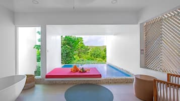 Une salle de bain moderne avec une grande baignoire, un banc rouge et une vue sur un jardin luxuriant, visible à travers une porte vitrée.