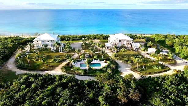 A large resort with two main buildings, a swimming pool, and a view of the ocean.