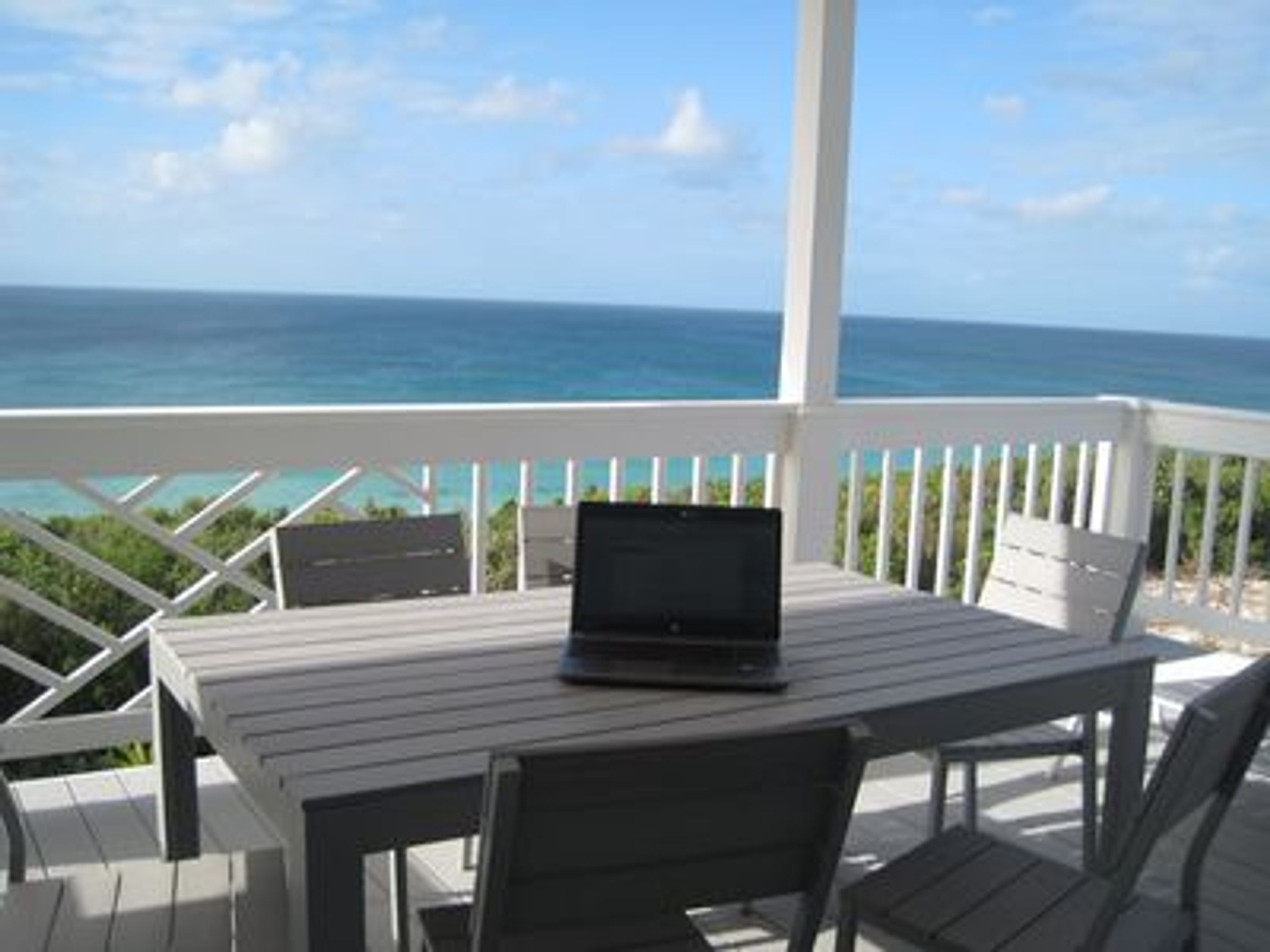 A balcony with a table and chairs, a laptop, and a view of the ocean.