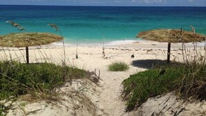 Une plage avec des parasols en chaume et une vue dégagée sur l’océan.