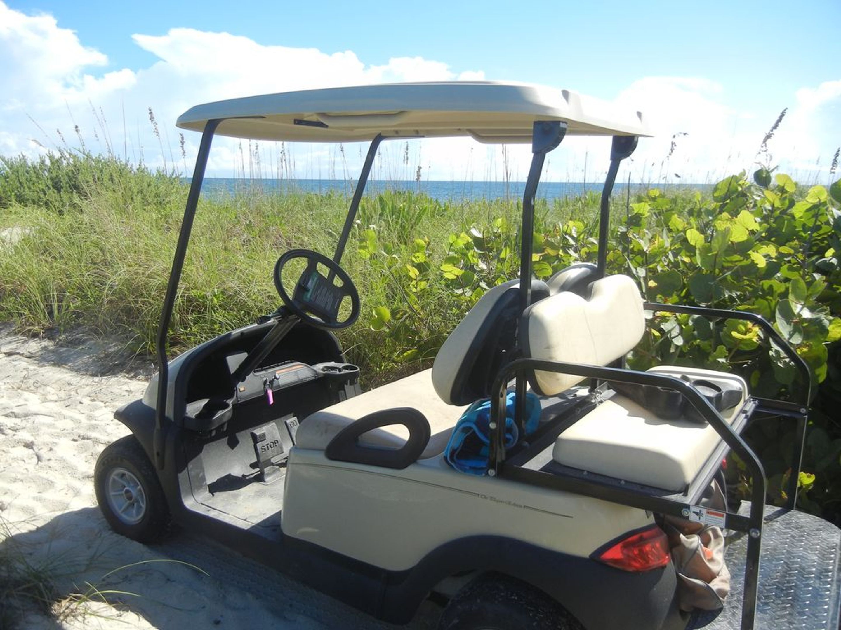 A golf cart parked on a sandy area with a view of the ocean and greenery in the background.