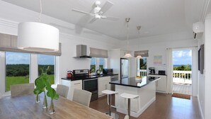 A modern kitchen with white cabinetry, a central island, and a dining area with a wooden table and chairs. - Buttonwood Reserve 1D (James Cistern)