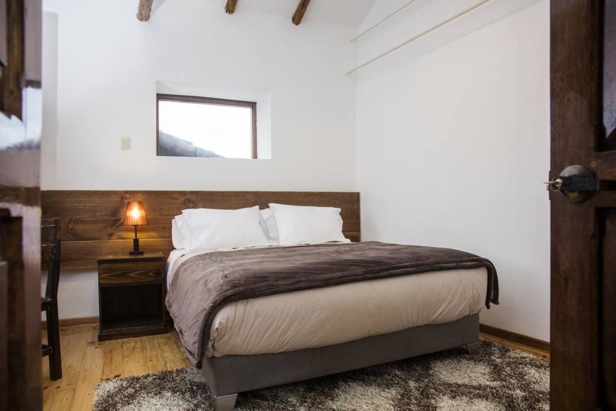 Une chambre à coucher avec un lit, une table de chevet, une lampe, une fenêtre et une porte.