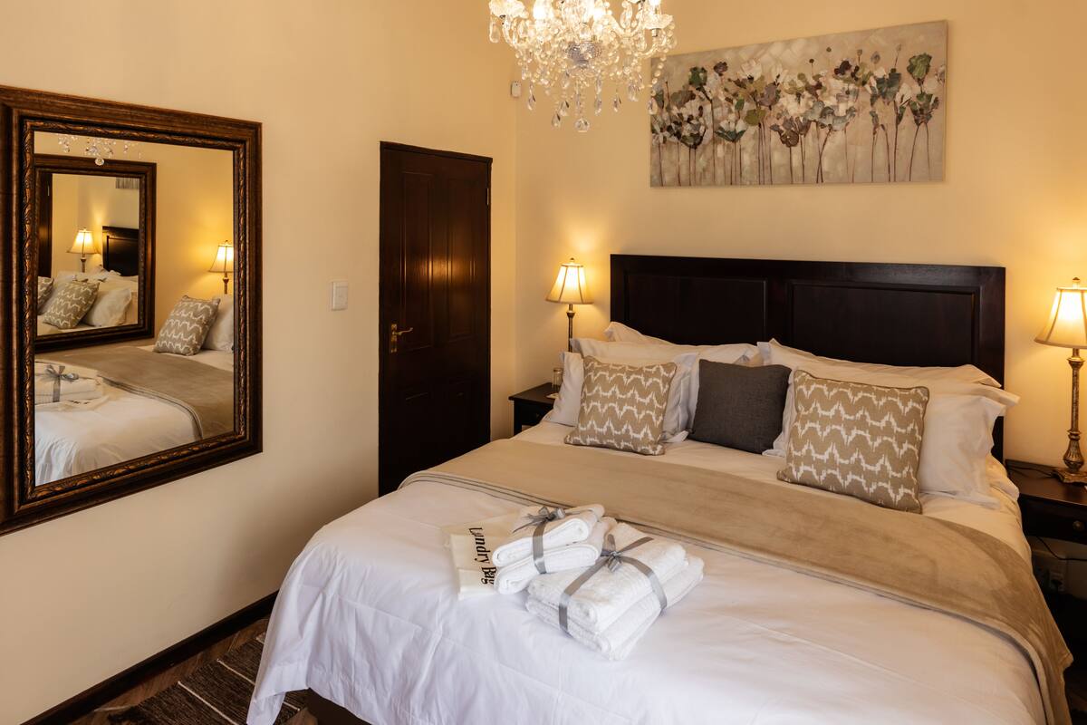 A neatly made bed with a headboard, a mirror, and a painting on the wall.