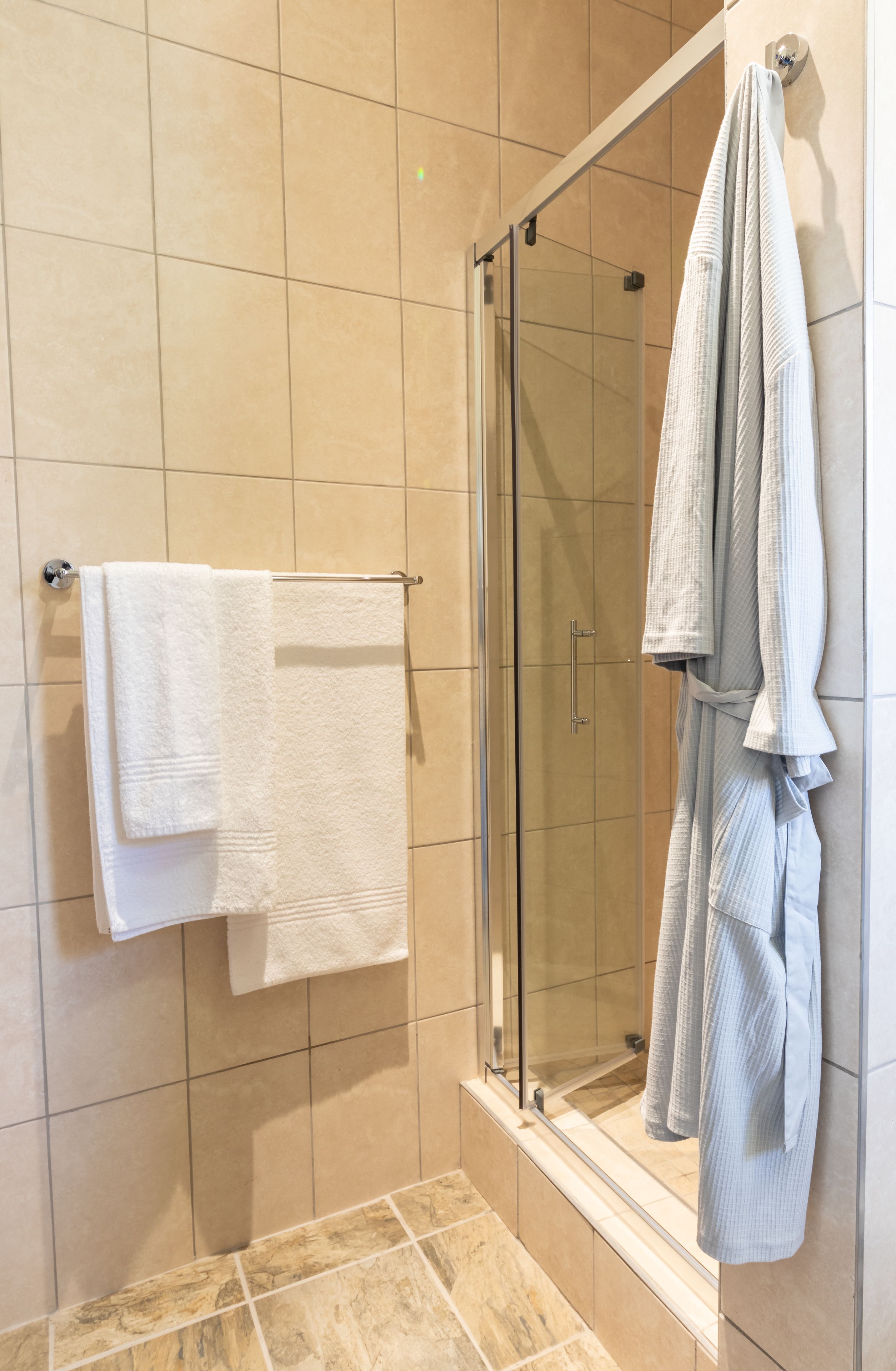 A bathroom with a glass shower enclosure, a white towel on a rack, and a robe hanging on the wall.