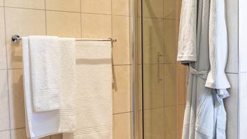 A bathroom with a glass shower enclosure, a white towel on a rack, and a robe hanging on the wall.