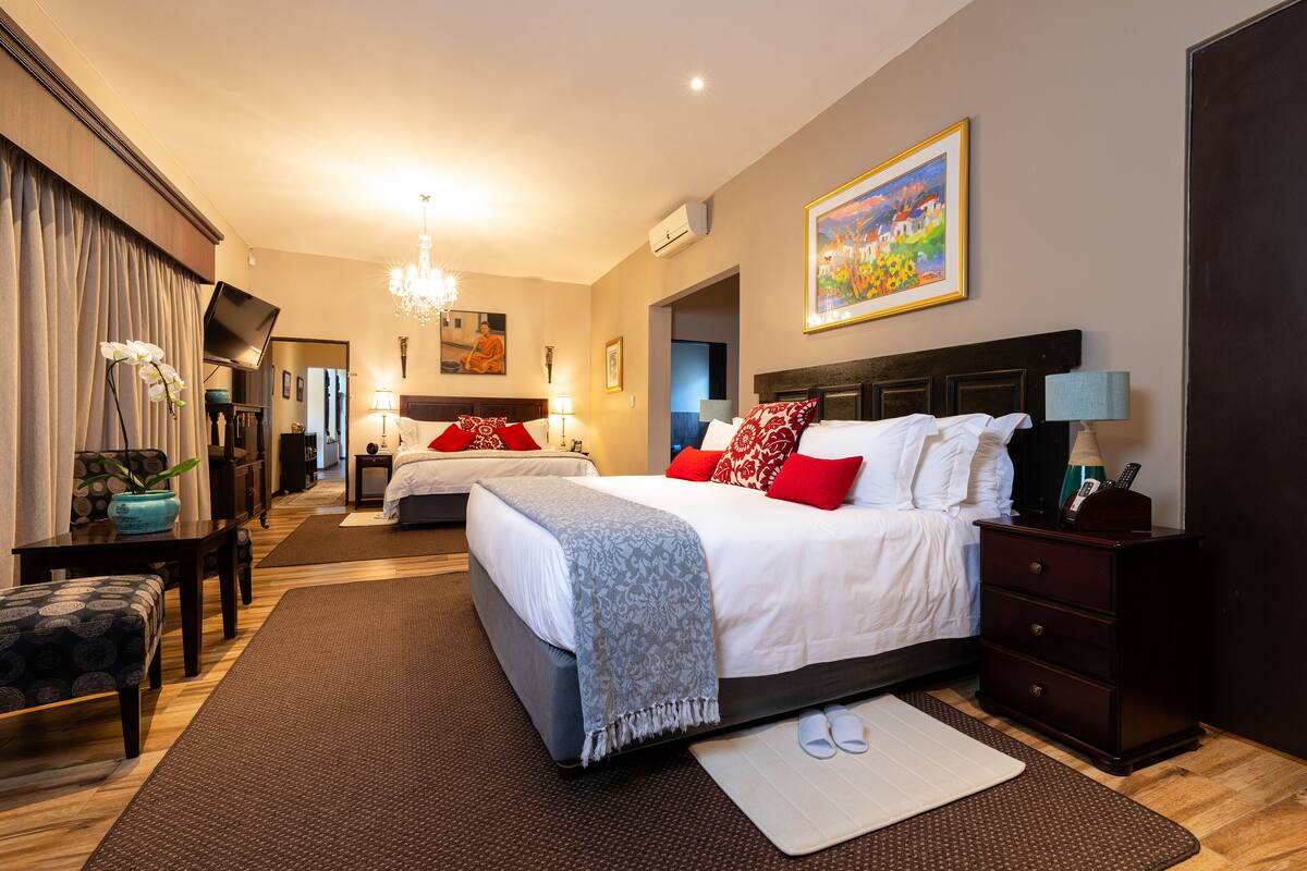 A hotel room with two beds, a desk, a chair, a TV, and a painting on the wall.
