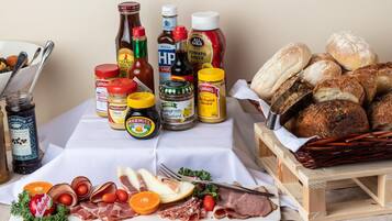 Uma mesa com diversos alimentos, incluindo carnes, queijos e acompanhamentos, além de uma cesta de pães.
