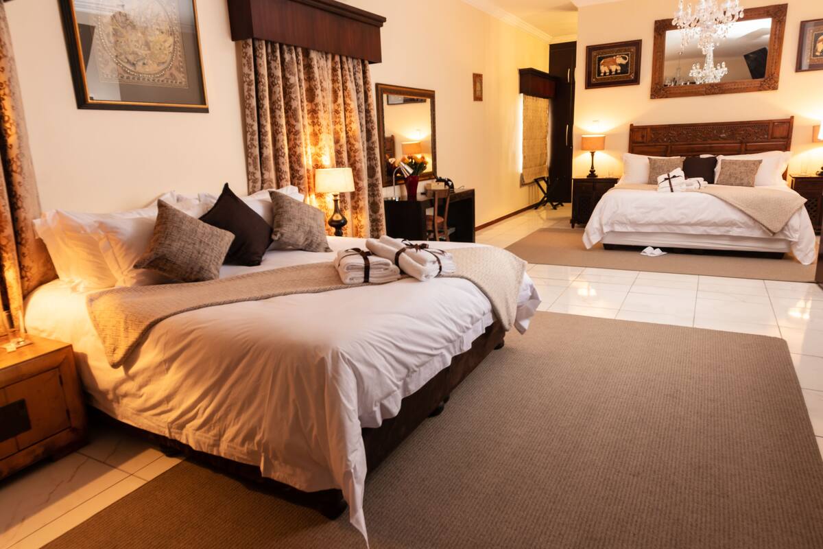 A hotel room with a large bed, a smaller bed, a desk, and a chair. There are two lamps on either side of the room.