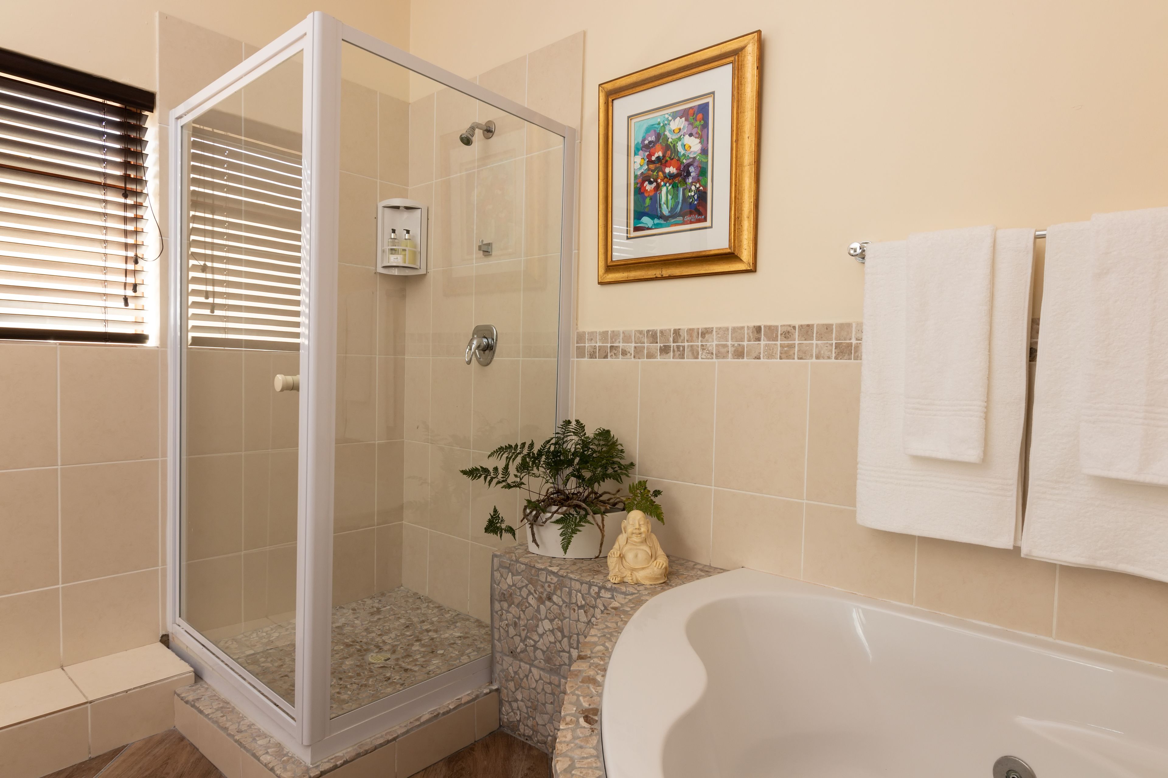 Ein Badezimmer mit einer gläsernen Duschkabine, einer Badewanne, einer Topfpflanze, einem gerahmten Kunstwerk und einem Handtuchhalter.