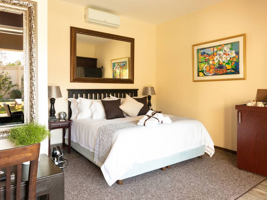 Camera d'albergo con un letto grande, una testiera in legno, un comodino con una lampada, una cassettiera, uno specchio e un quadro appeso al muro.