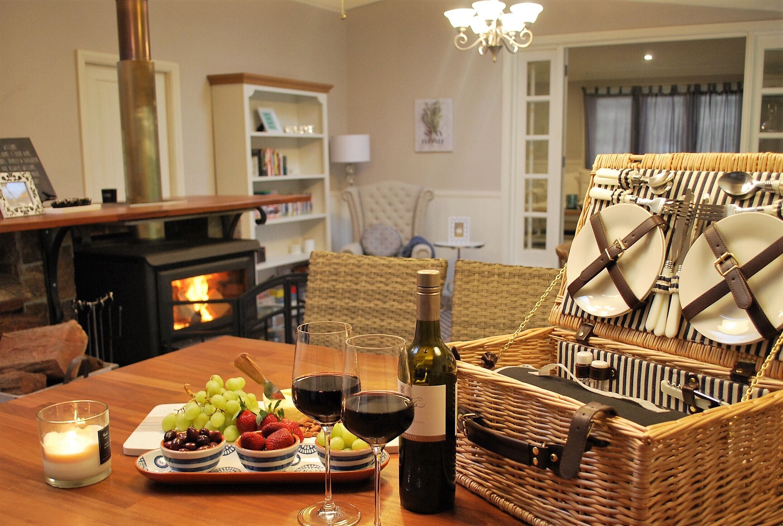 A cozy dining area with a wooden table set for a meal, a wine bottle, and a basket of cutlery.