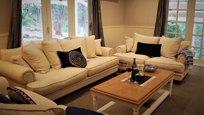 A living room with two beige sofas, a wooden coffee table, and a view of a forest through large windows. - Mount Tomah Huntington Lodge - peaceful & picturesque Hamptons styled hideaway  (Mount Tomah)