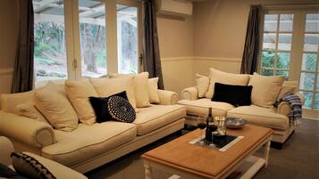 A living room with two beige sofas, a wooden coffee table, and a view of a forest through large windows.