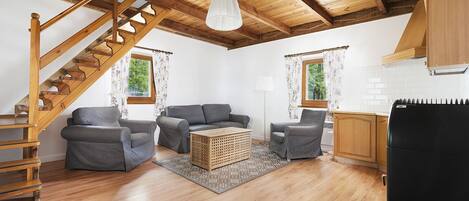 A cozy living room with a wooden staircase, grey sofas, a coffee table, and a black refrigerator.