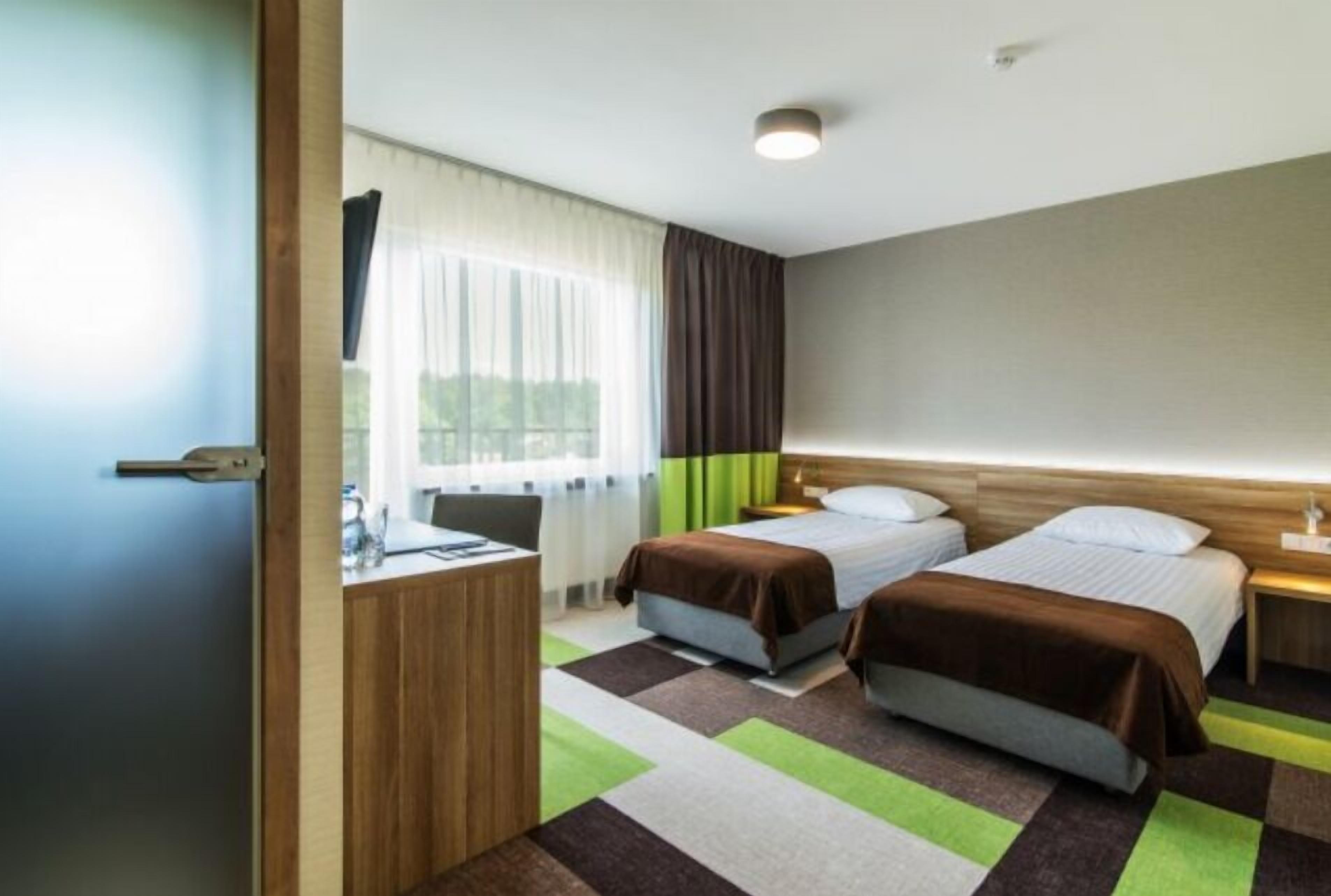 A hotel room with two beds, a desk, and a window with curtains.
