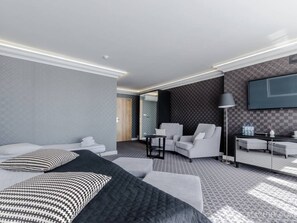 A modern hotel room with a bed, two sofas, a small table, a TV, and a lamp. - Mazurski Raj Hotel Marina & Spa (Ruciane-Nida)