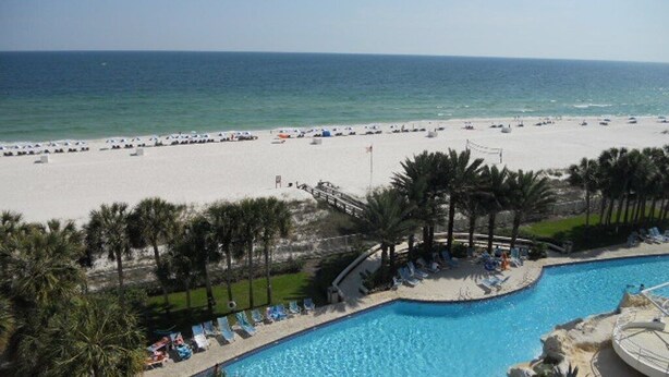 A beach resort with a swimming pool, palm trees, and a sandy beach. - Gulf Front Condo with Stunning Views! (Pensacola)