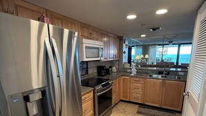 A modern kitchen with stainless steel appliances, wooden cabinets, and a view of the ocean. - Gulf Front Condo with Stunning Views! (Pensacola)