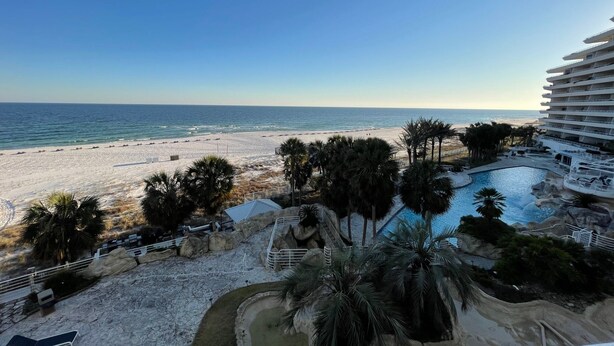 A beach resort with a pool, palm trees, and a view of the ocean.