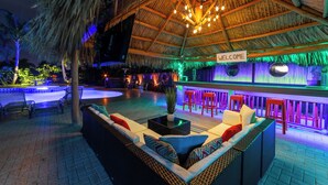 An outdoor bar area with a thatched roof, wicker furniture, and a 'WELCOME' sign.