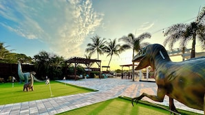 A golf course with dinosaur statues, a pergola, palm trees, and a brick pathway.