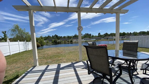 A covered patio with a table and chairs, overlooking a lake and residential area.