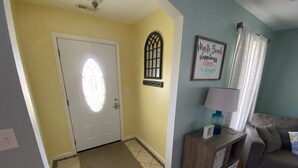 A living room with a door, a wall-mounted lamp, a couch, and a rug.