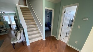A spacious living area with a wooden floor, a staircase, and a dining area with chairs and a table.