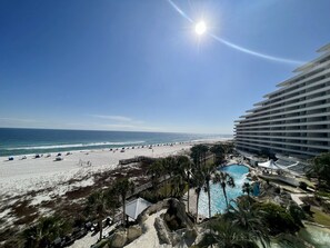 A beach resort with a pool, palm trees, and a large hotel building.