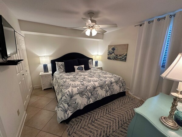 A bedroom with a bed, nightstands, a ceiling fan, a wall-mounted TV, and a painting.