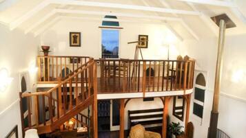 A cozy loft bedroom with a wooden staircase, a piano, and a cozy seating area.