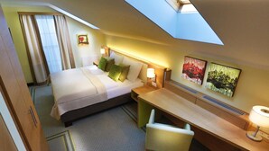 Quarto de hotel com cama, escrivaninha, cadeira e obras de arte nas paredes.