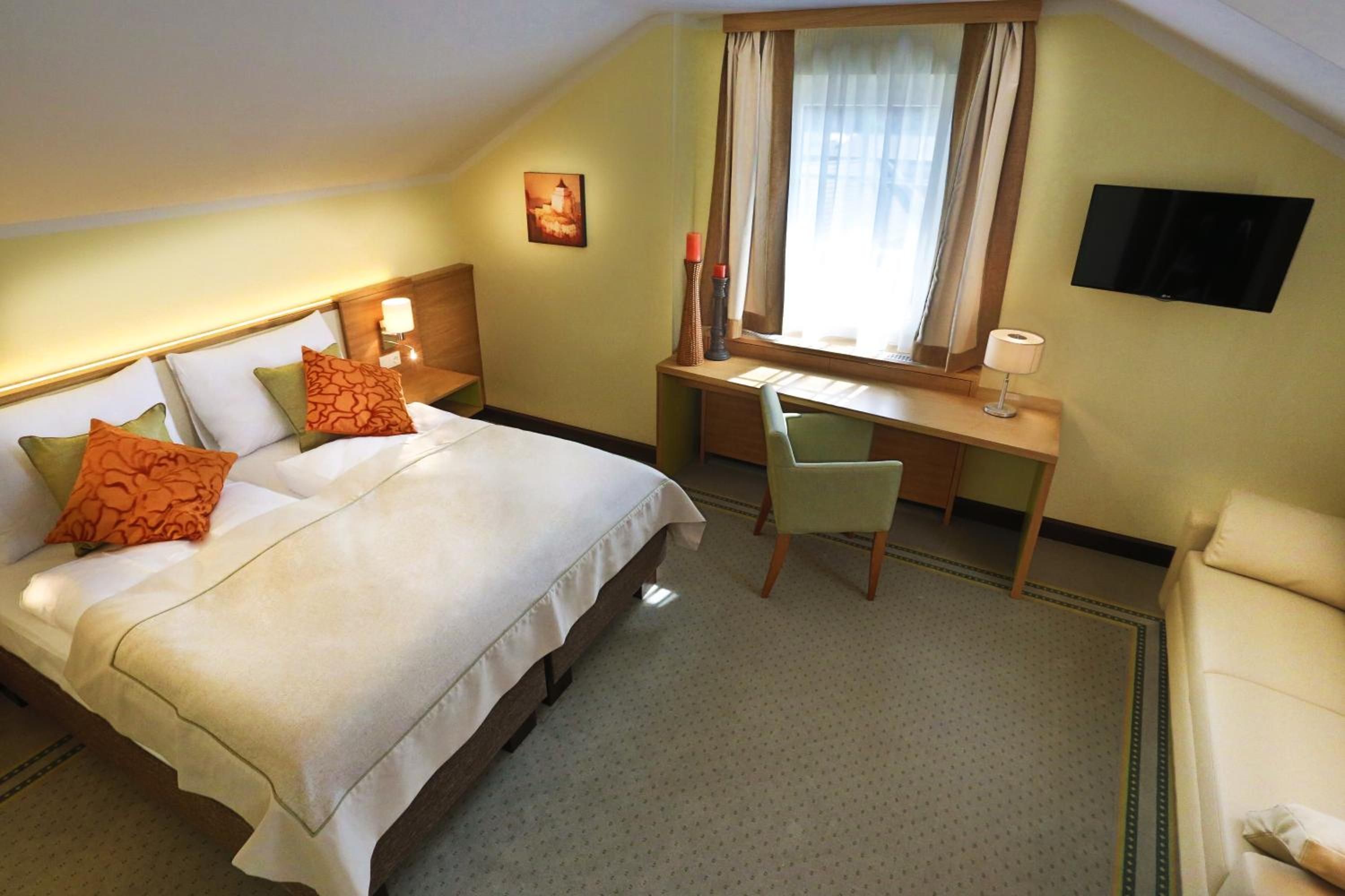 A hotel room with a bed, a desk, a chair, a television, and a window with curtains.