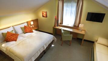 A hotel room with a bed, a desk, a chair, a television, and a window with curtains.
