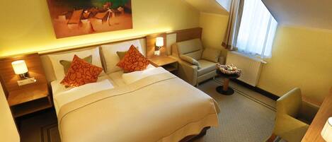 A hotel room with a bed, a chair, a desk, and a painting on the wall.