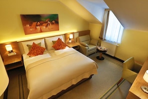 Quarto de hotel com cama, cadeira, escrivaninha e um quadro na parede.