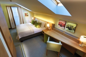 Quarto de hotel com cama, escrivaninha, cadeira e obras de arte nas paredes.