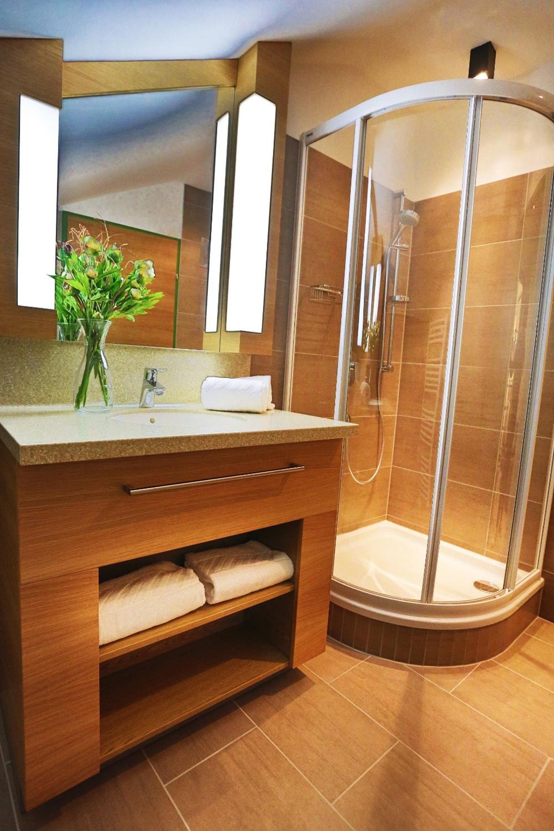 A modern bathroom with a wooden vanity, a glass shower enclosure, and a mirror above the sink.