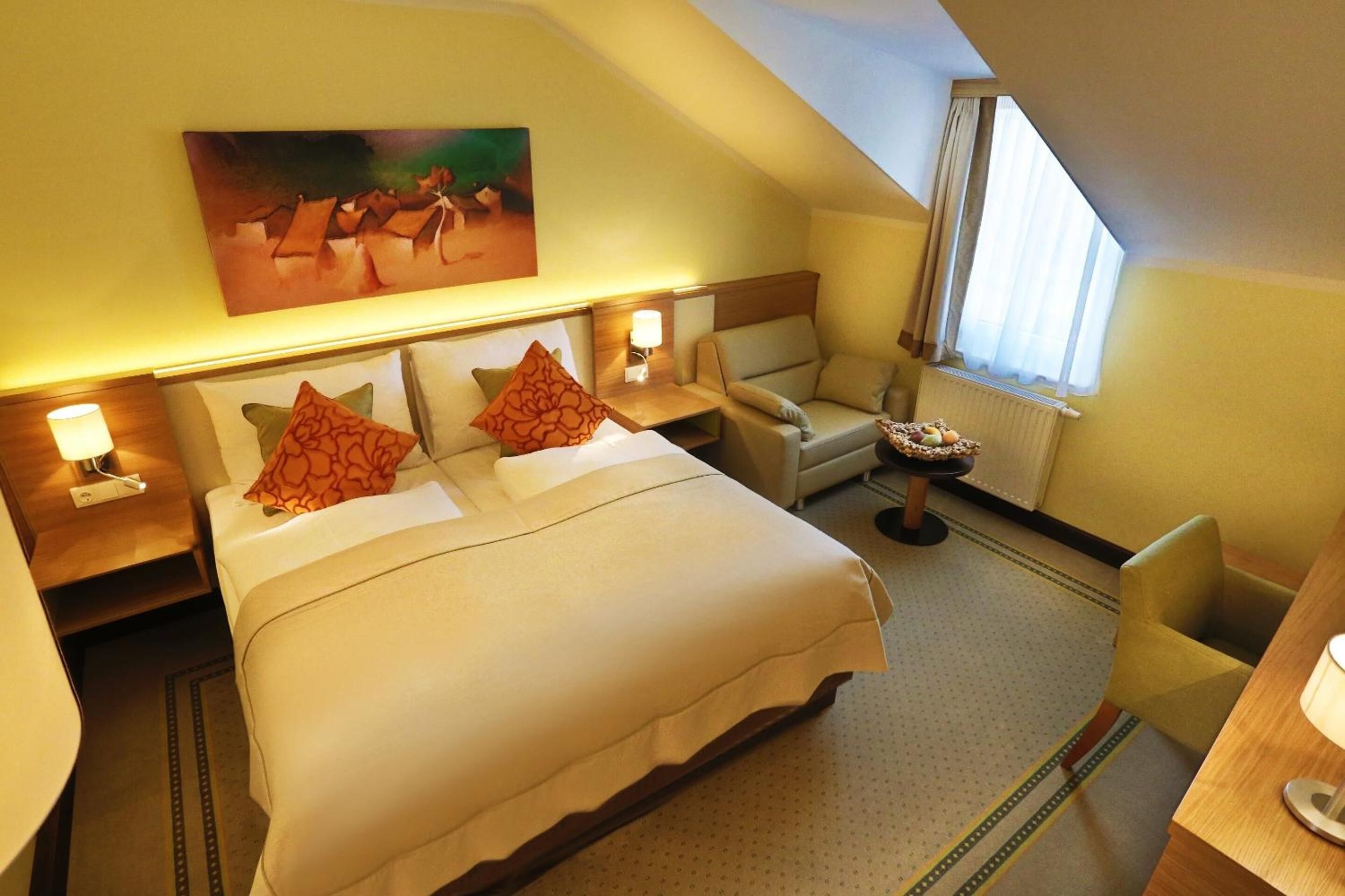 Une chambre d’hôtel avec un lit, une chaise, un bureau et un tableau au mur.