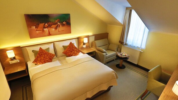 Quarto de hotel com cama, cadeira, escrivaninha e um quadro na parede.