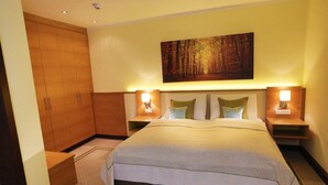 Quarto de hotel com uma cama grande, duas mesas de cabeceira com abajures, um guarda-roupa e um quadro na parede.