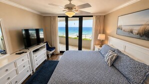 Ein Hotelzimmer mit Bett, Fernseher, Deckenventilator, einem Balkon mit Meerblick und einem Bild an der Wand.