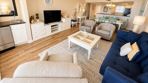 Ein Wohnzimmer mit Fernseher, einer Couch, Sesseln und einem Essbereich mit Tisch und Stühlen.
