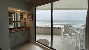 Een balkon met uitzicht op de oceaan, een eethoek met stoelen, en een keuken met kastjes en een spoelbak.